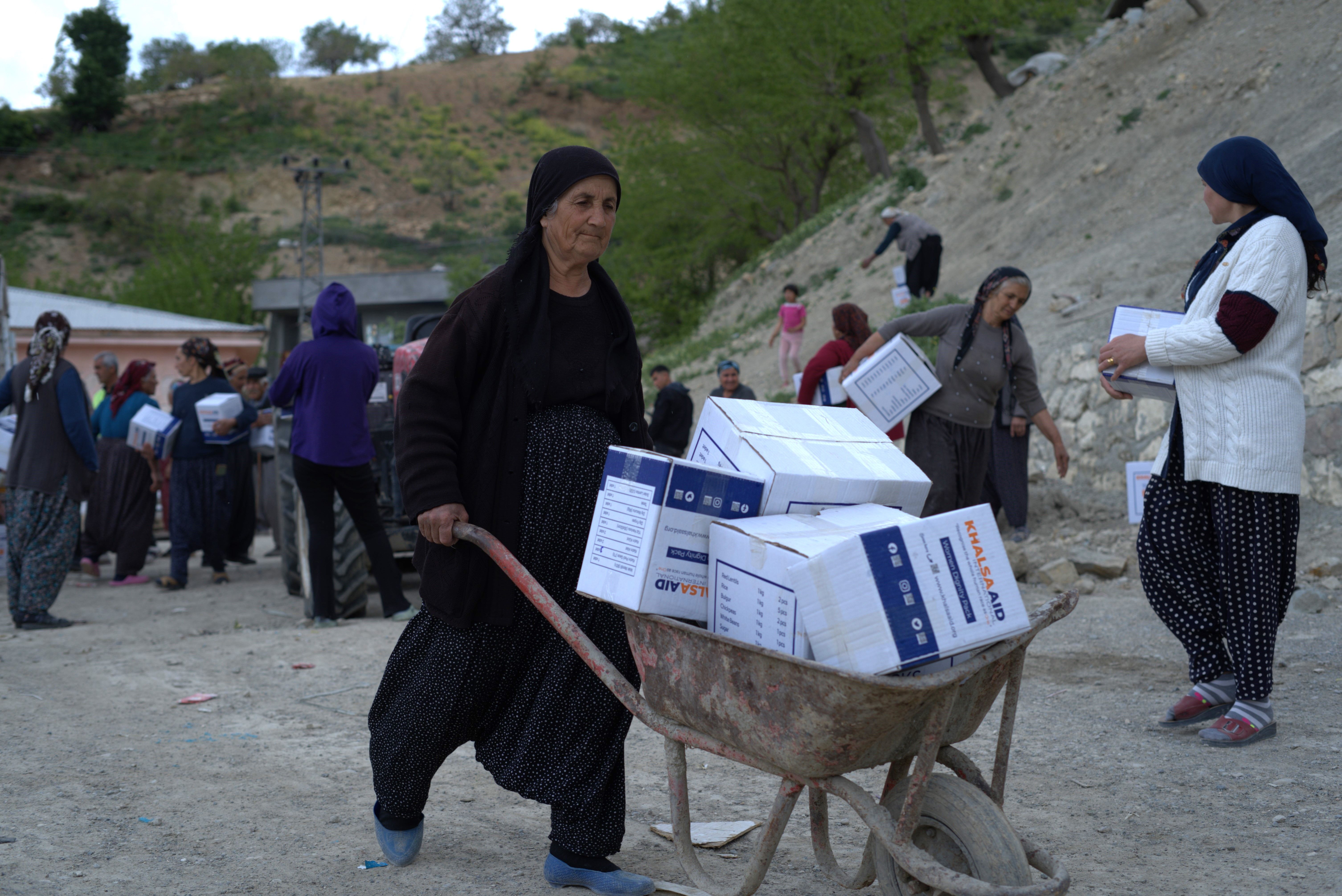 Iraqi ladies resolutely pushing a wheelbarrow of distributed Khalsa Aid Dignity Packs. 